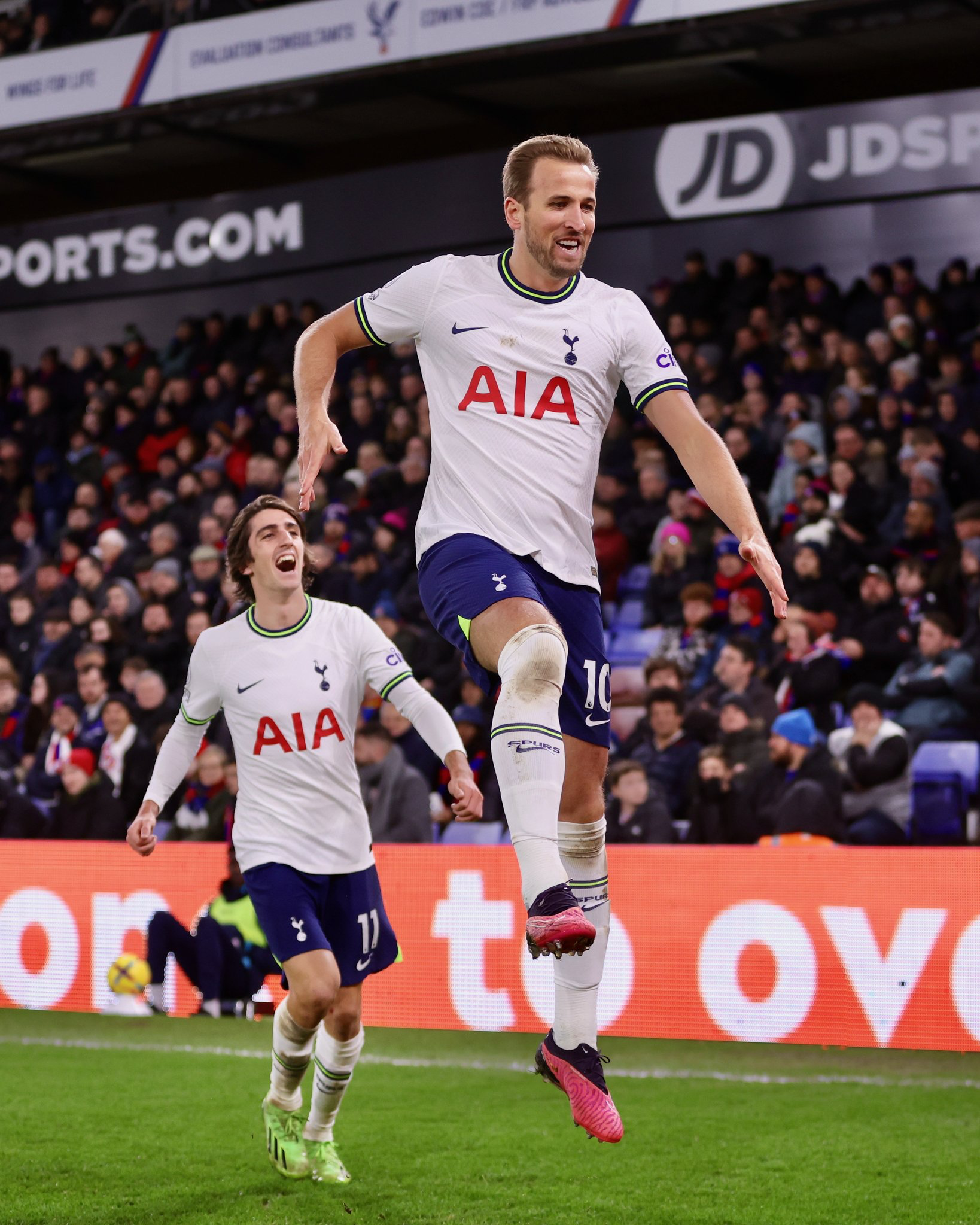 Harry Kane leaps to celebrate a goal while Bryan Gil looks on joyfully in the background