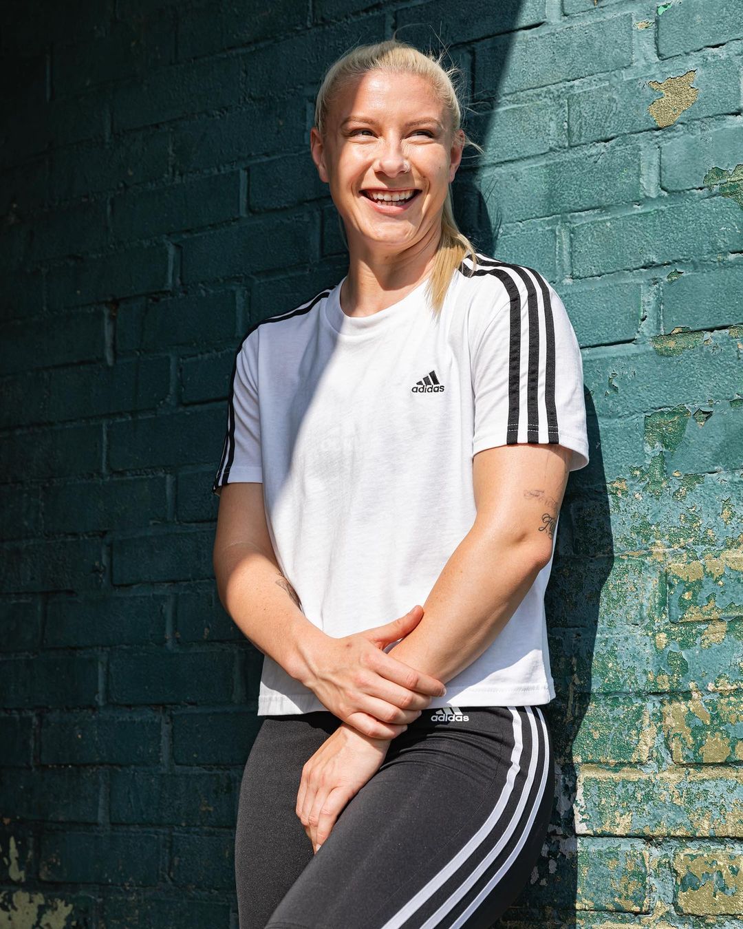 Beth England leans against a green brick wall in an all-Adidas outfit