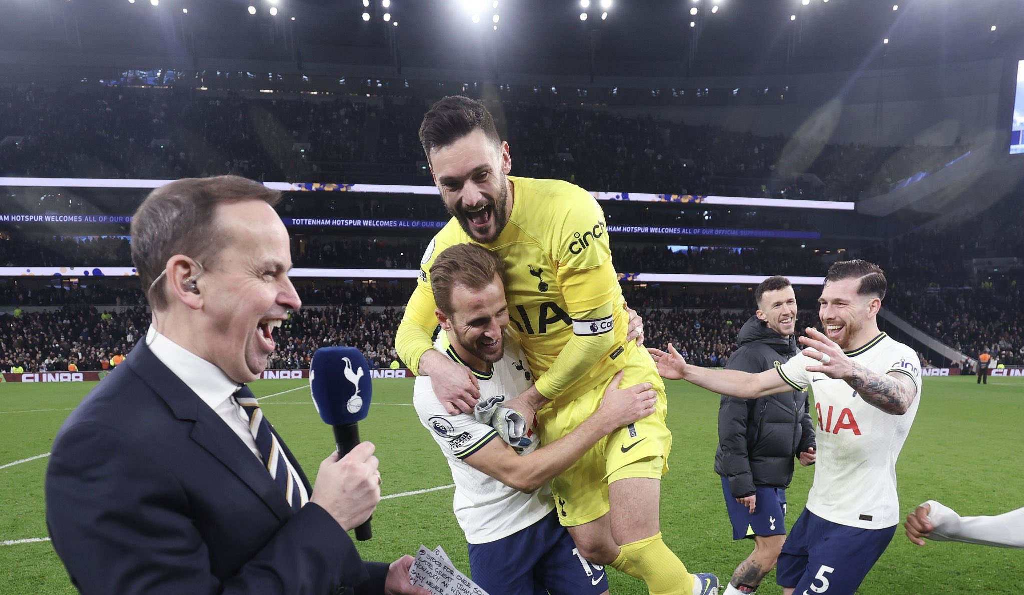 Hugo Lloris jumps onto Harry Kane while celebrating the latter's record goal, as Pierre-Emile Højbjerg approaches with arms open from the side.