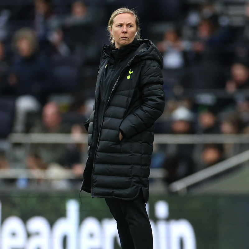 Rehanne Skinner stands on the touchline during a Spurs Women match, slightly frowning.