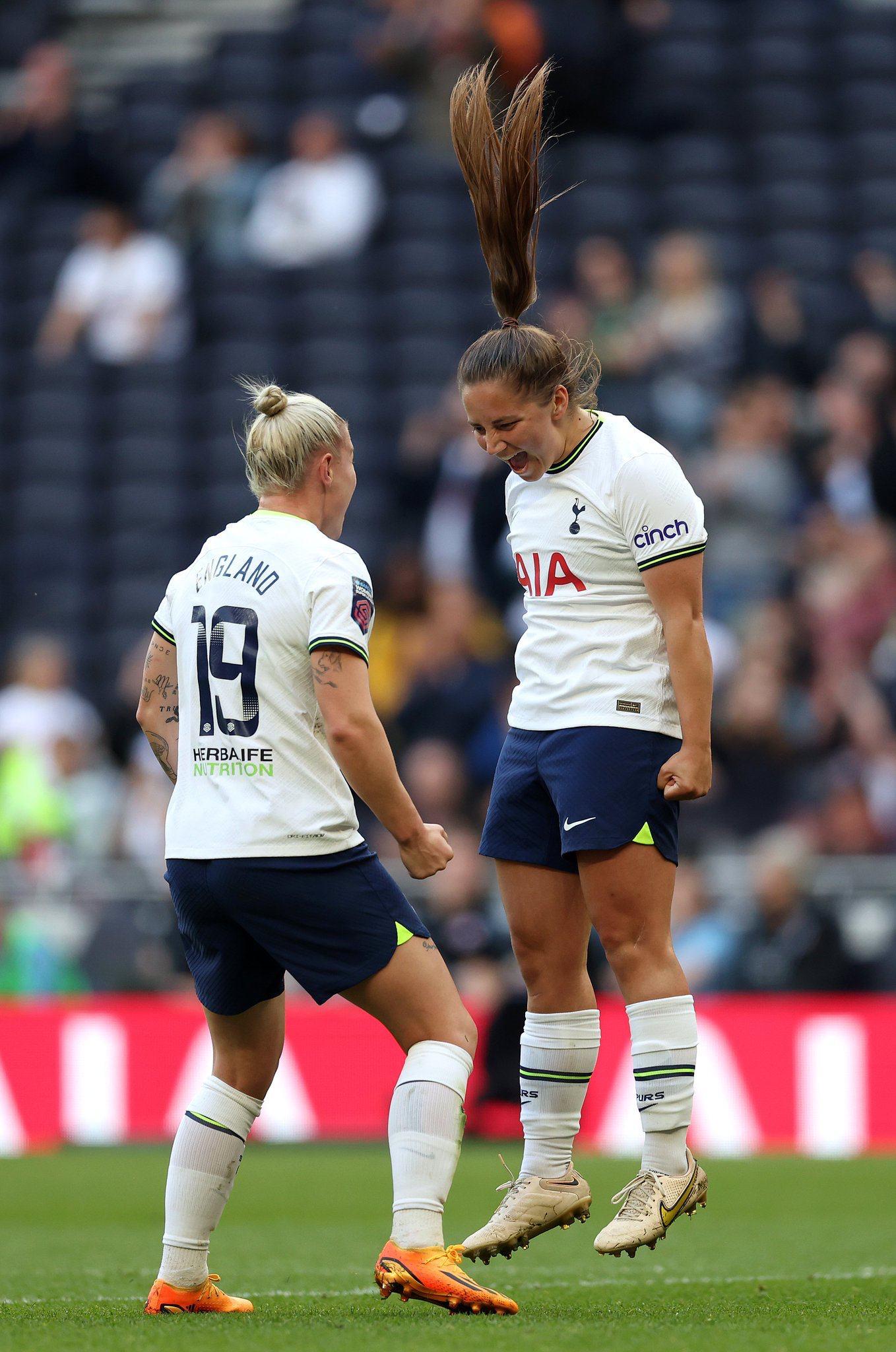 Kit Graham jumps into the air to celebrate in front of Beth England, her ponytail flying high.