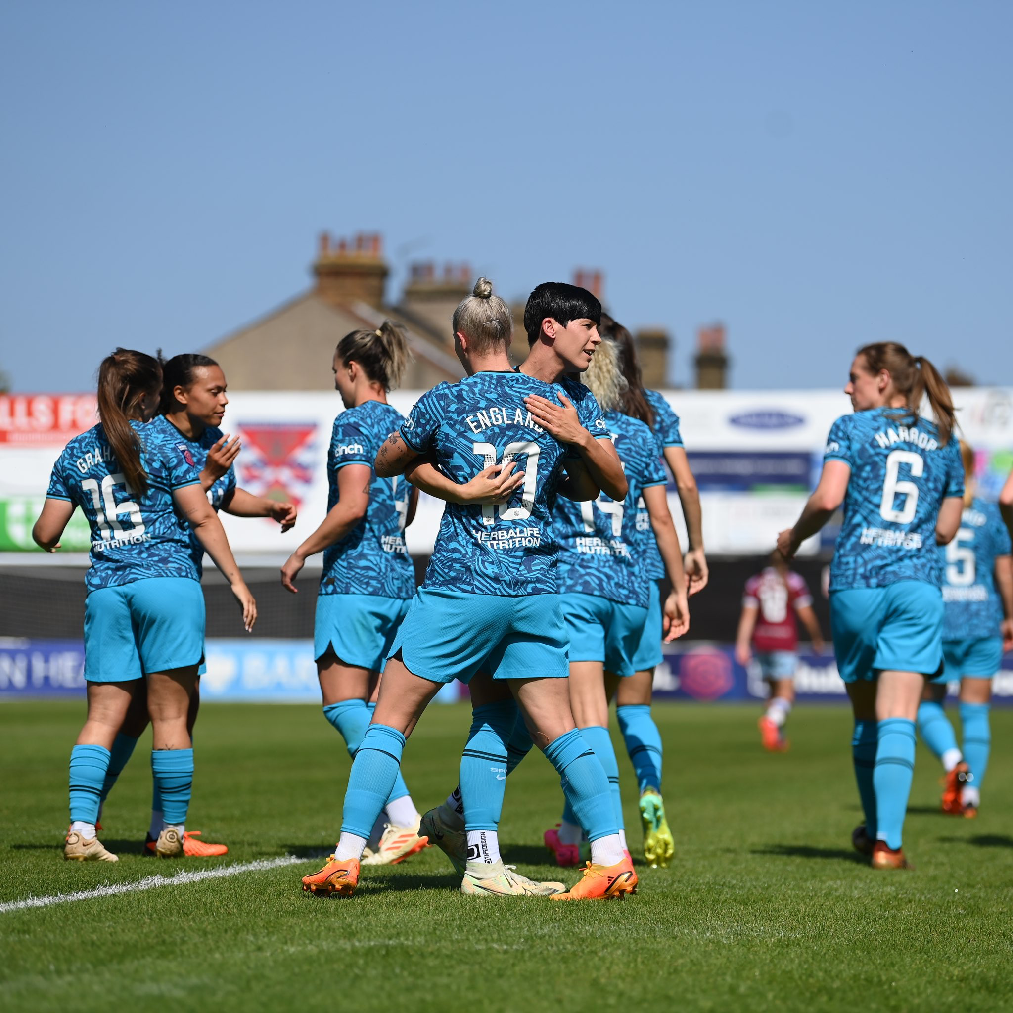 Beth England and Ash Neville celebrate in the foreground while several teammates flank them in the background.