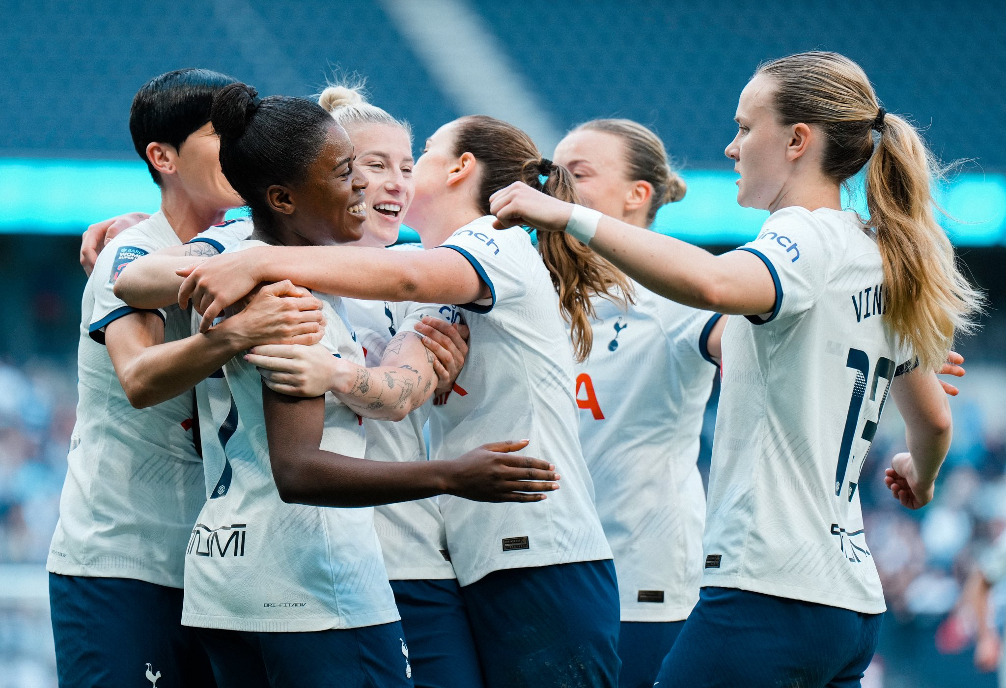 Several Spurs Women players hug each other and smile after a goal.