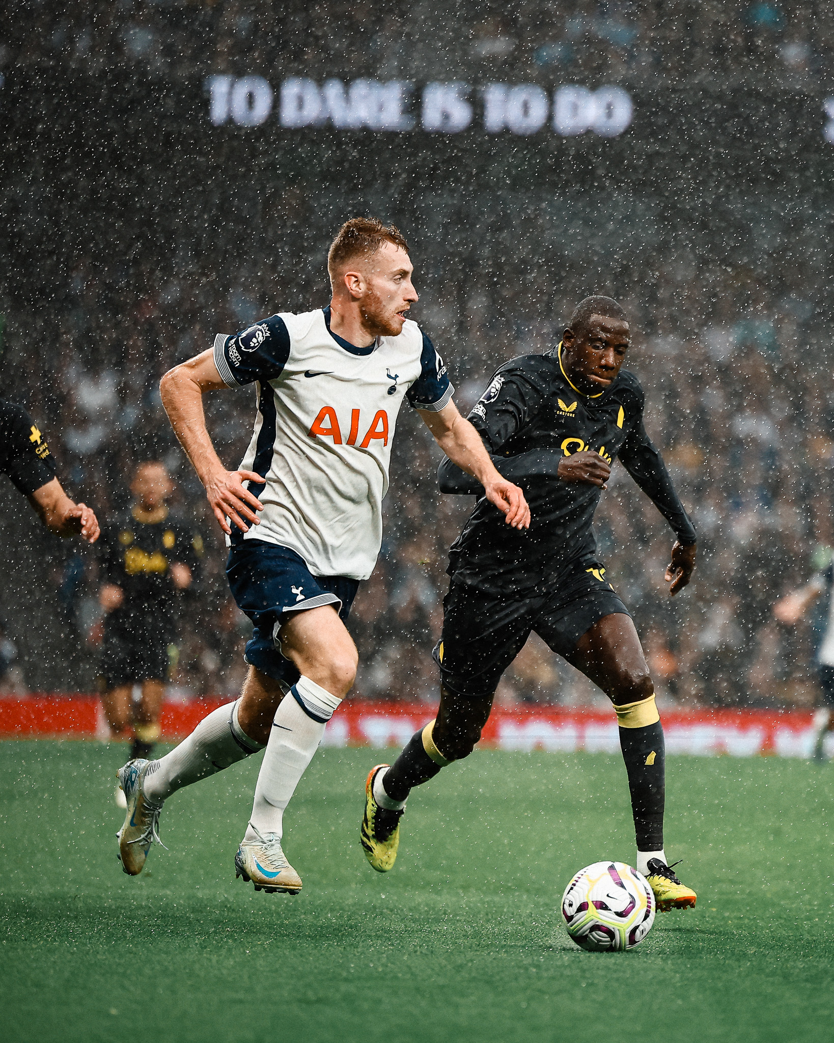 Dejan Kulusevski dribbles with the ball in the rain as an Everton player approaches.