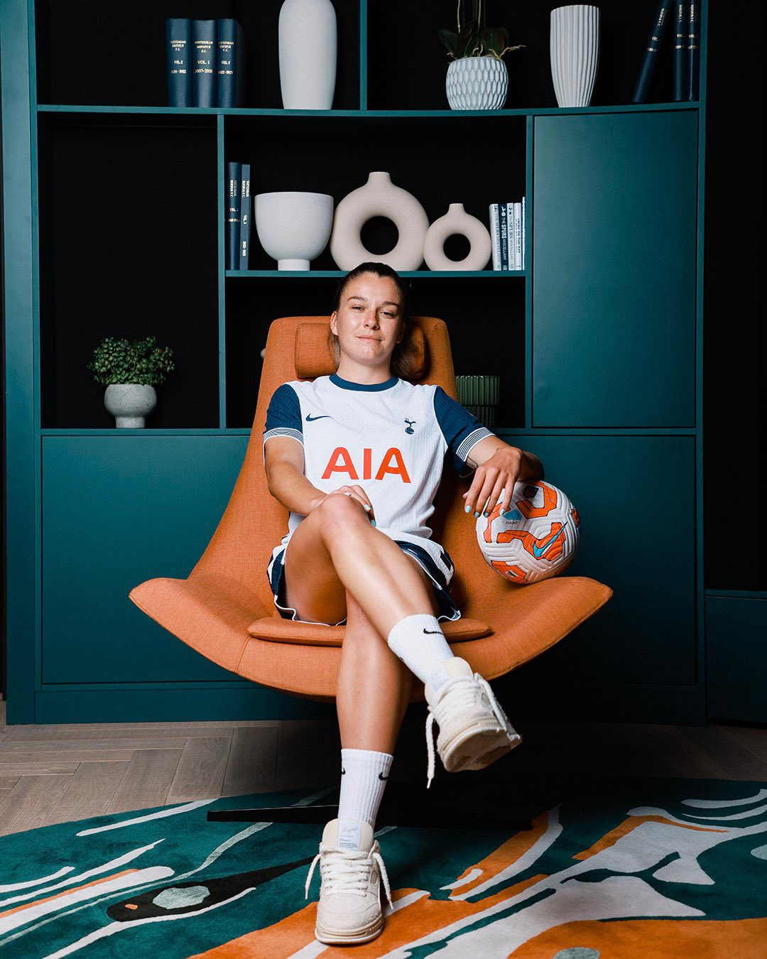 Anna Csiki poses with a soccer ball on a retro orange chair.