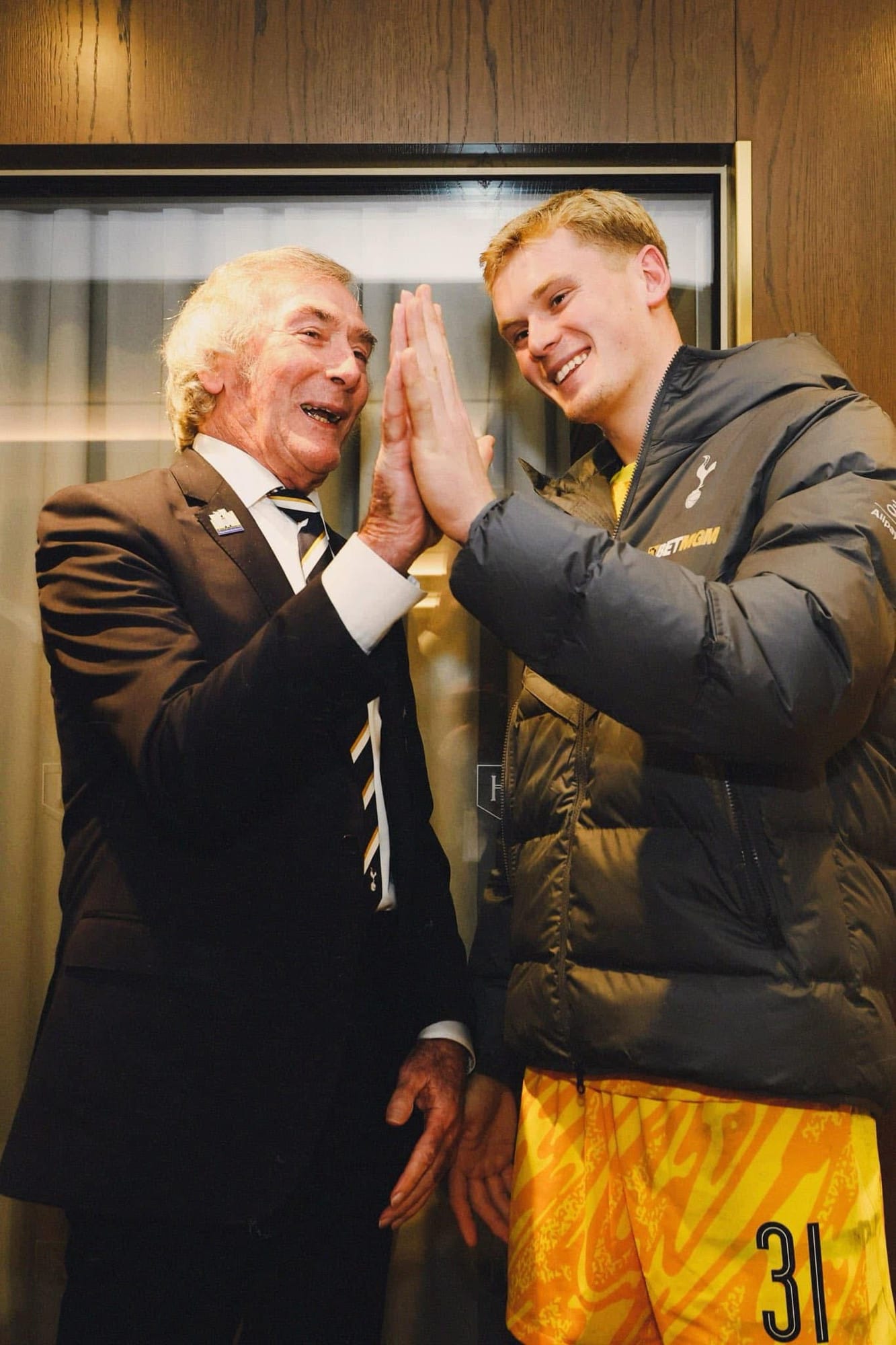 Pat Jennings and Antonín Kinský compare their hand size by high fiving, both smiling widely.