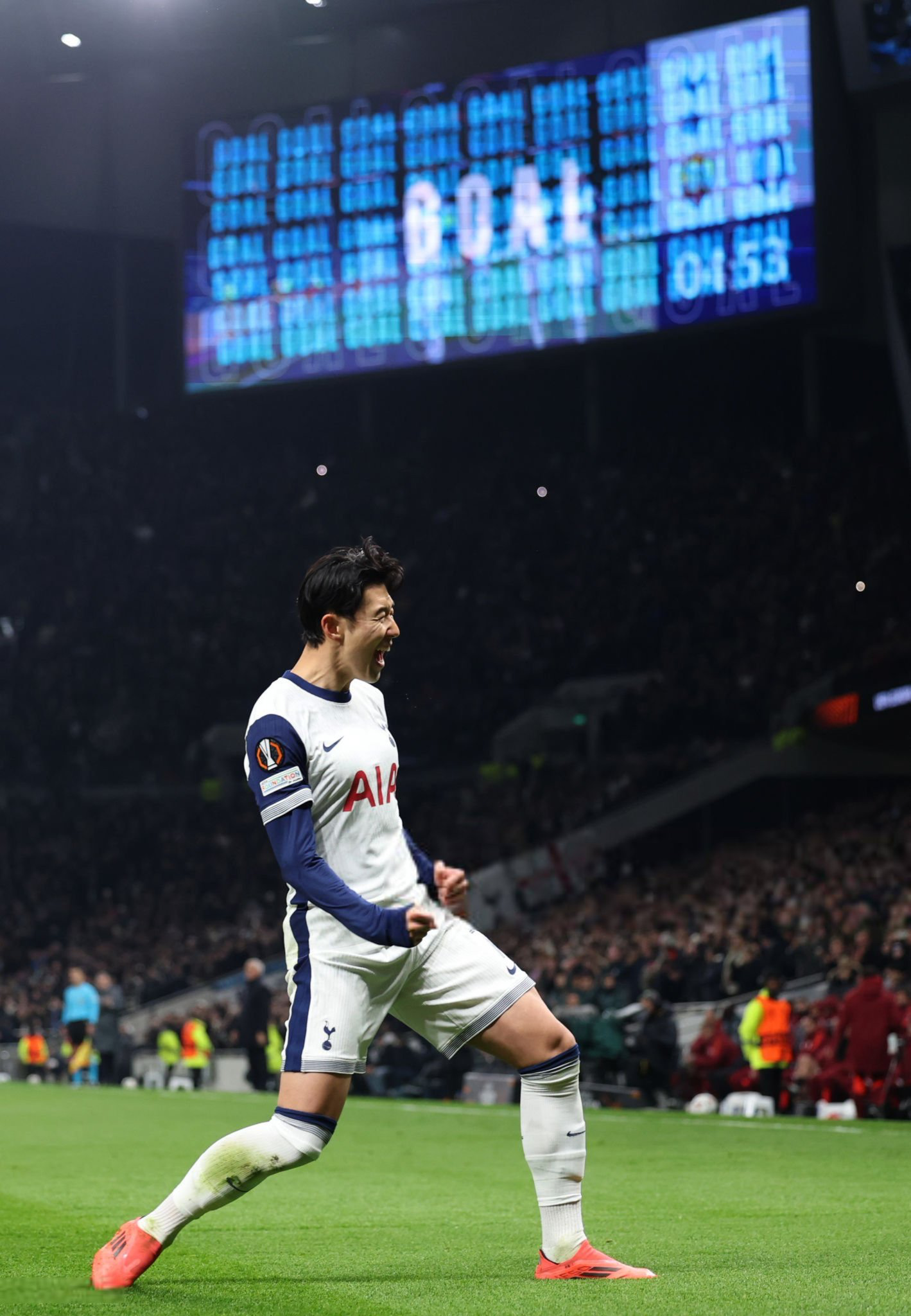 Son Heung-min celebrates a goal with the videoboard showing "goal" above him.