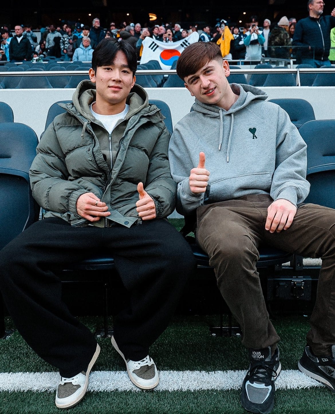 Yang Min-hyeok and Mikey Moore give a thumbs up while sitting on the sideline in their street clothes.