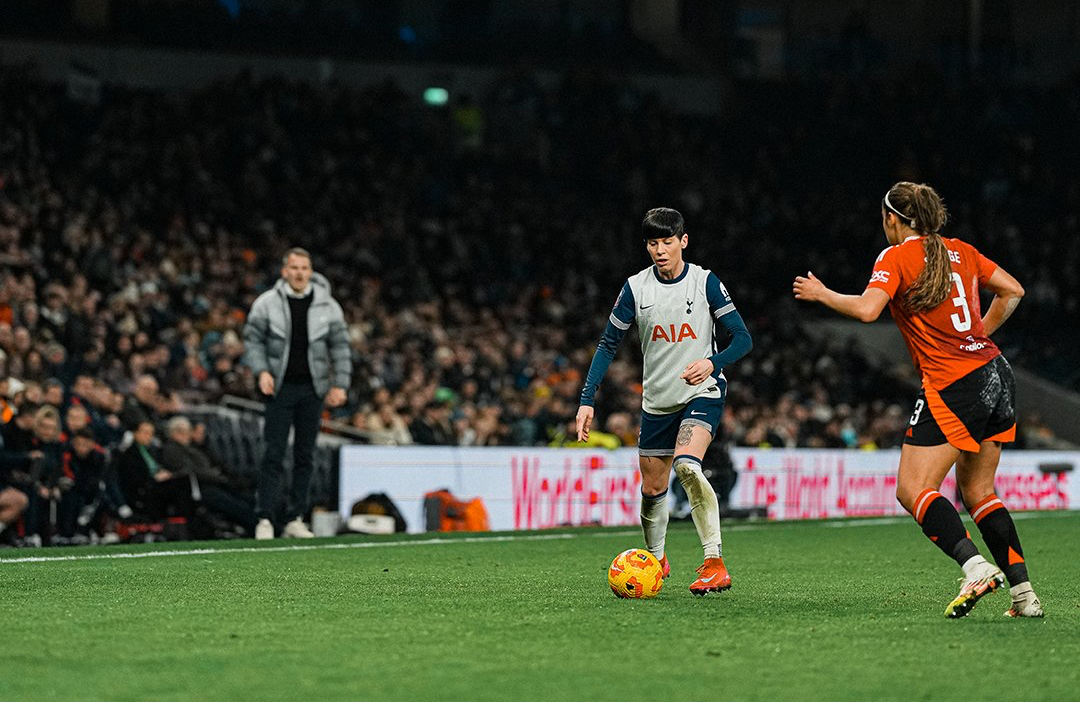 Ash Neville dribbles the ball with Gabby George approaching and Robert Vilahamn shouting instructions from the touchline.