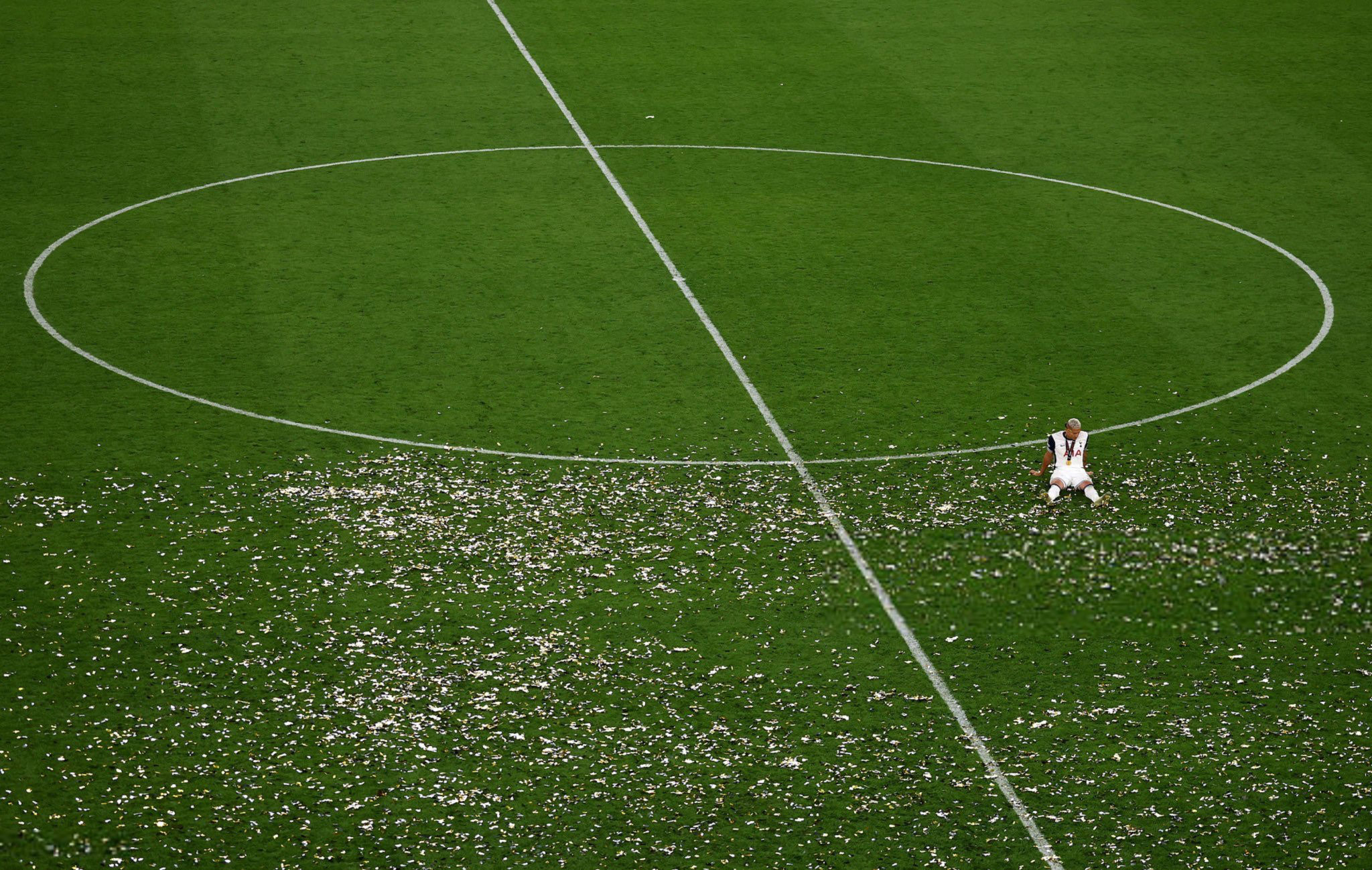 Richarlison sits alone on the empty pitch with confetti surrounding him.
