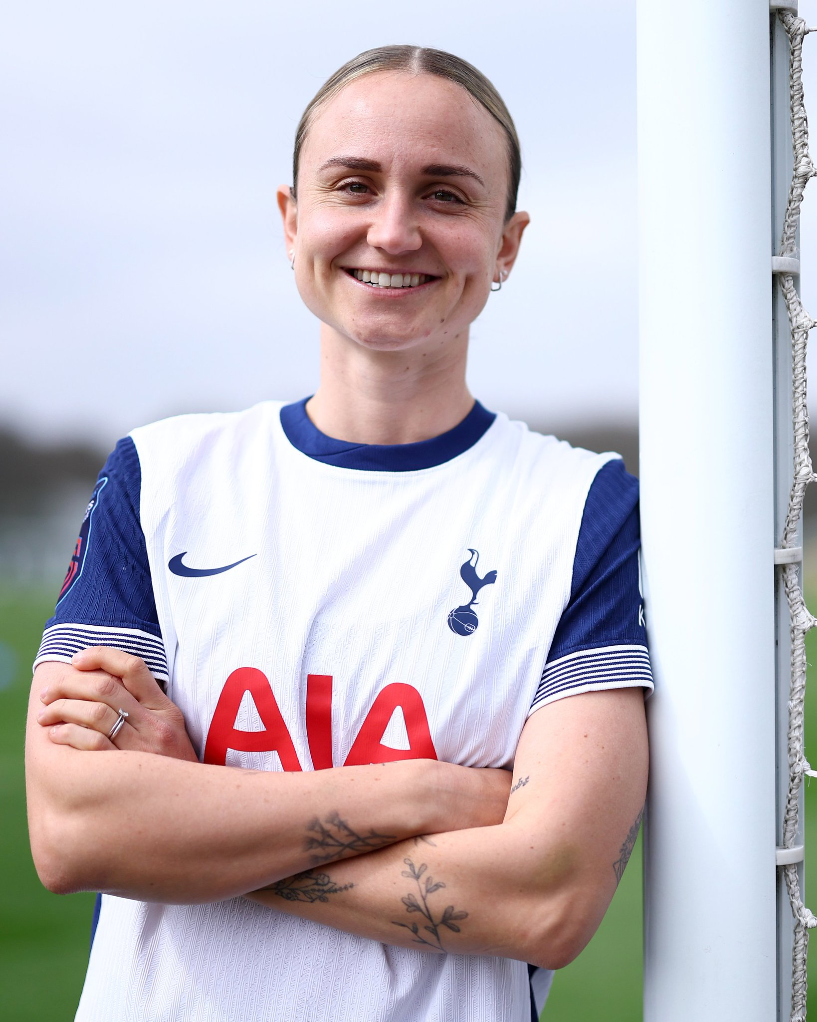 Martha Thomas leans against a goal post with her arms crossed and smiles.