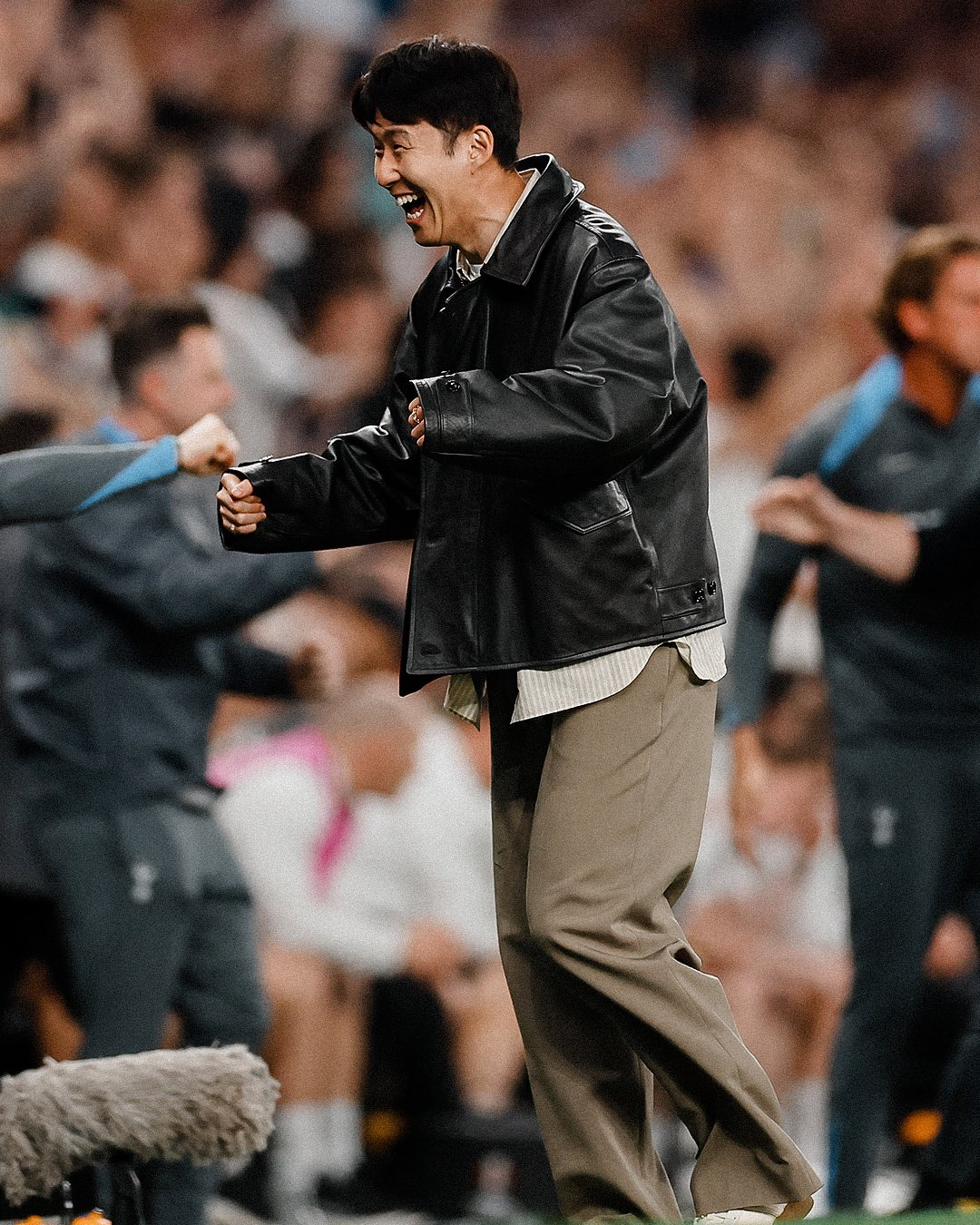 Son Heung-min stands up to celebrate a goal from the sideline in his street clothes.