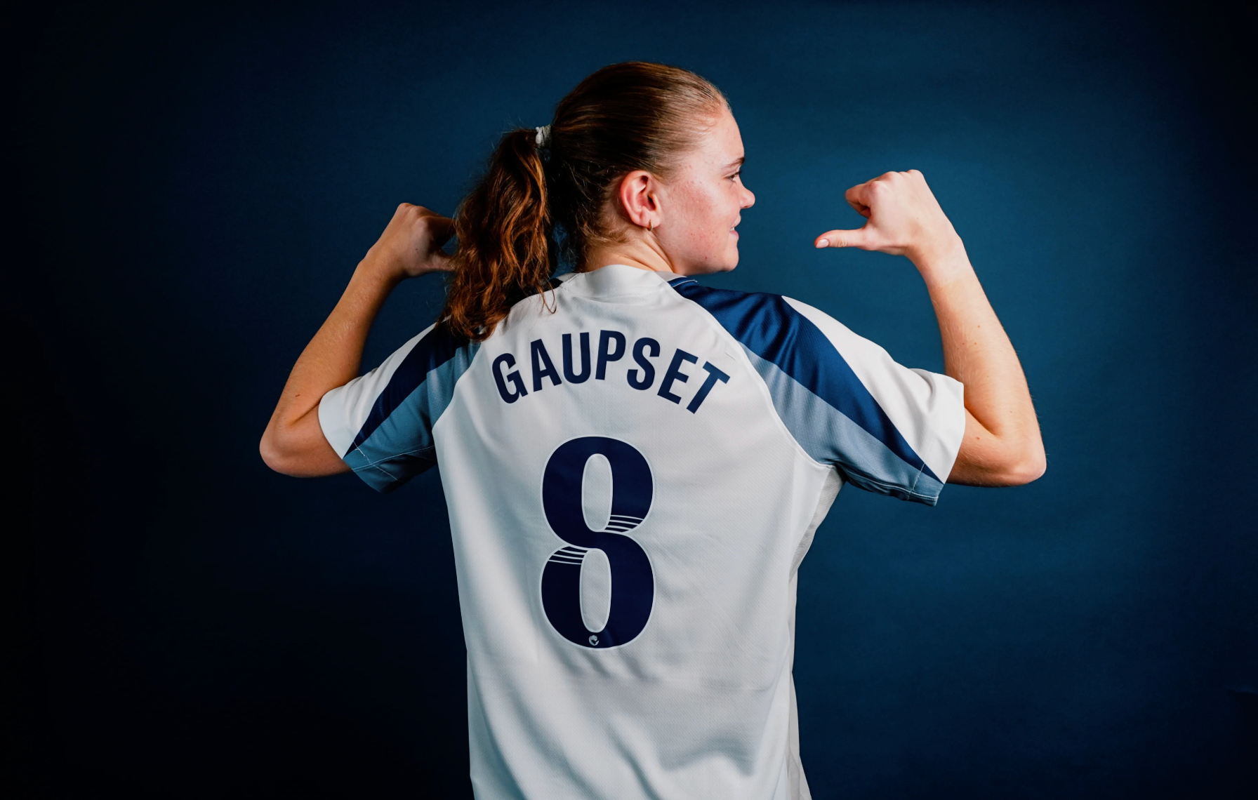Signe Gaupset points with both thumbs over her shoulders to her name and number eight on her new Spurs kit.