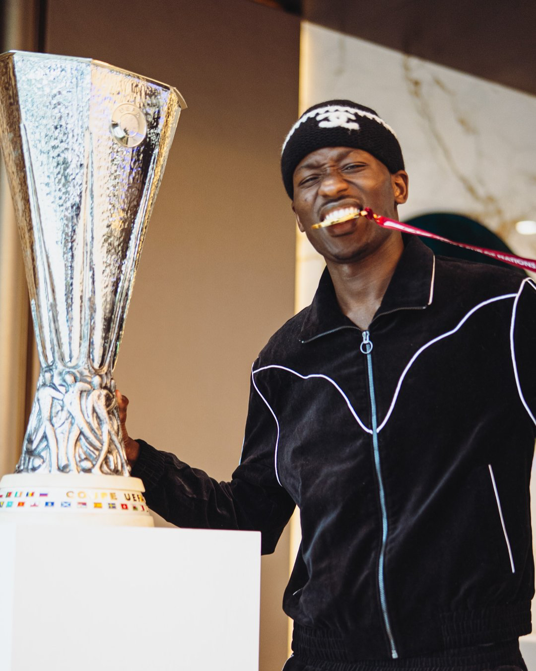 Pape Sarr poses with the Europa Leauge trophy, his AFCON winners medal clamped between his teeth.