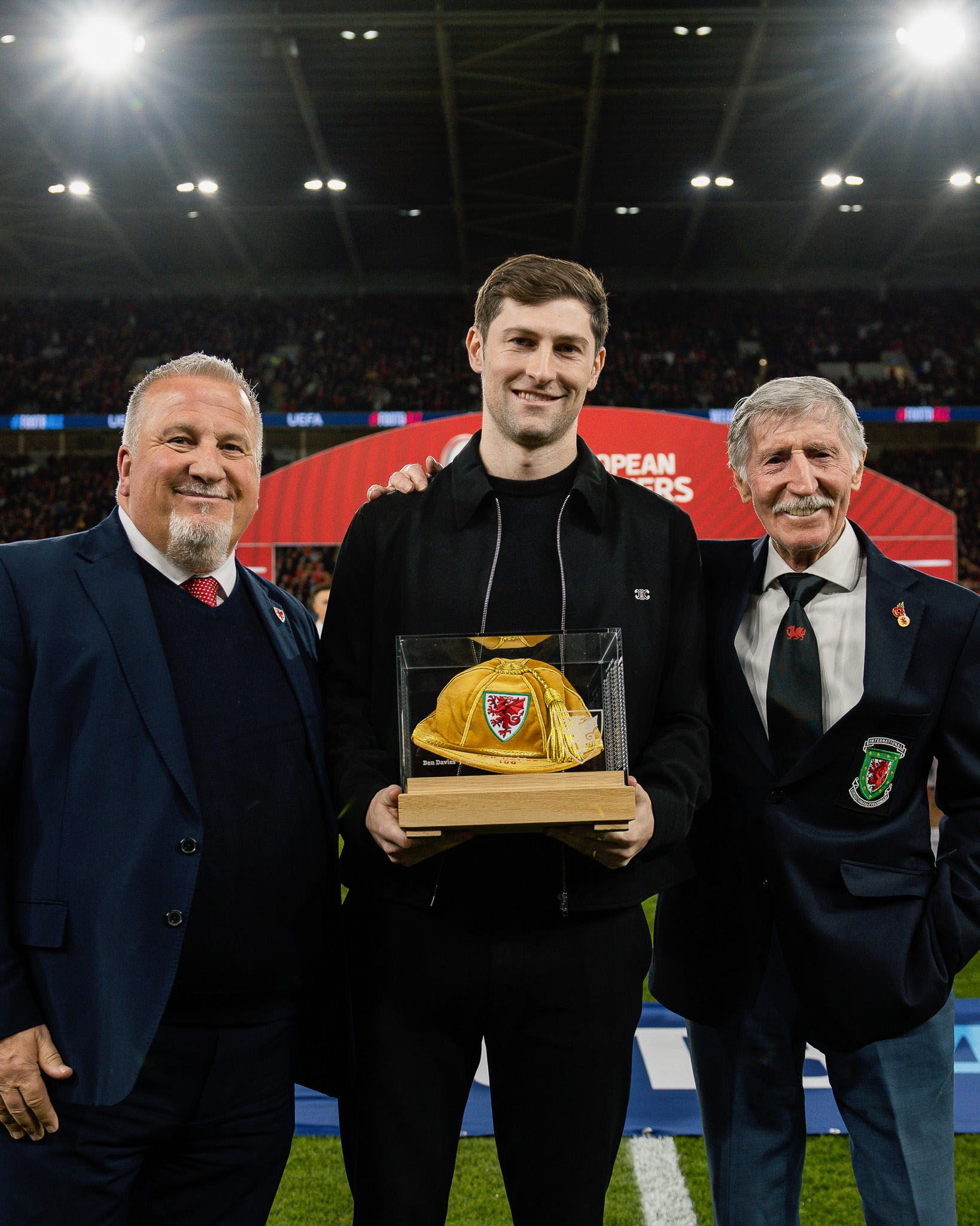 Ben Davies holding up his 100th Wales cap commemoration, while Cliff Jones puts an arm around his shoulder.