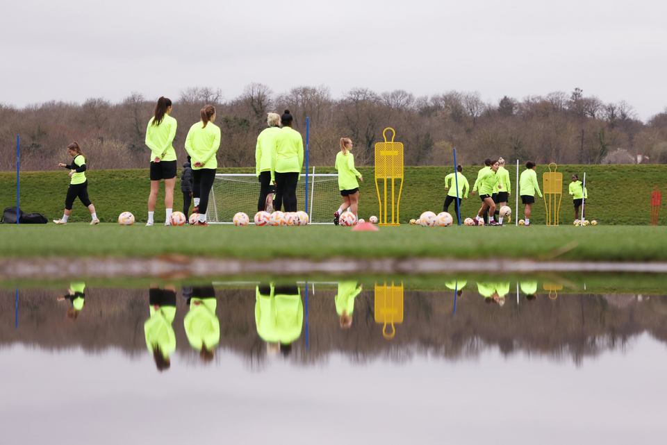 Several Spurs Women players train near a body of water reflecting them. 