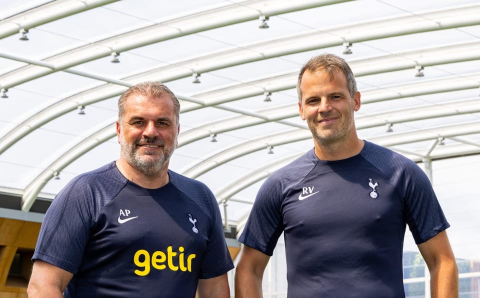 Ange Postecoglou and Robert Vilahamn stand side by side in the training center in blue Spurs gear, smiling.