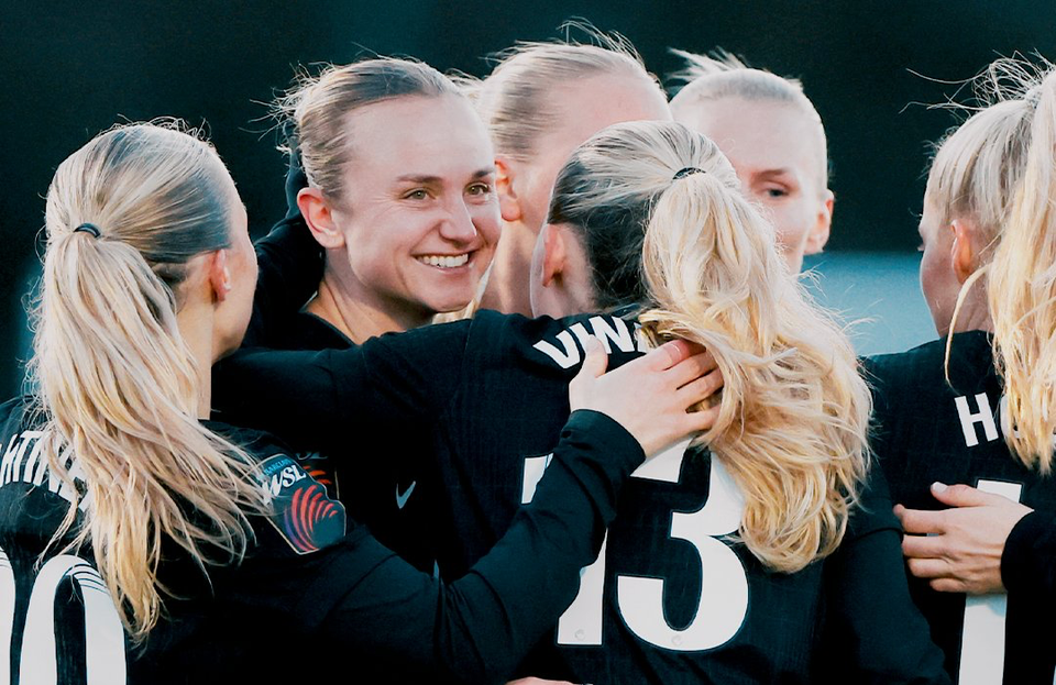 Martha Thomas grins broadly after scoring her first goal of the season, surrounded by teammates.
